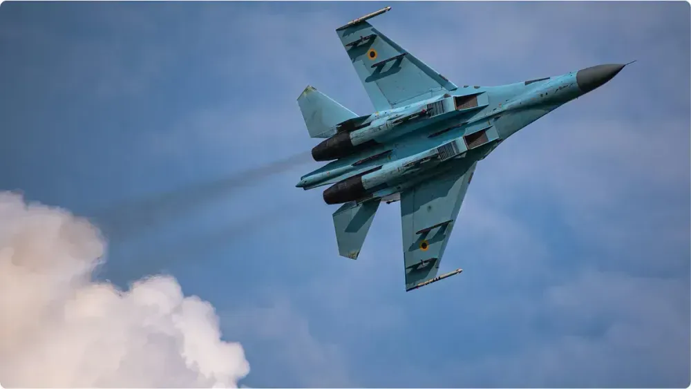 Український винищувач Су-27 виконує різкий віраж на фоні хмарного неба, з двома двигунами на форсажі. На хвостовому оперенні та крилі видно розпізнавальні знаки Повітряних Сил ЗСУ.